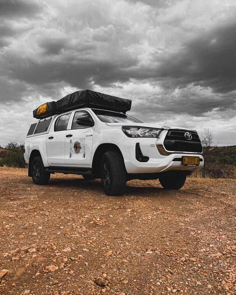 A white Toyota Hilux double cab with a rooftop tent on a gravel surface