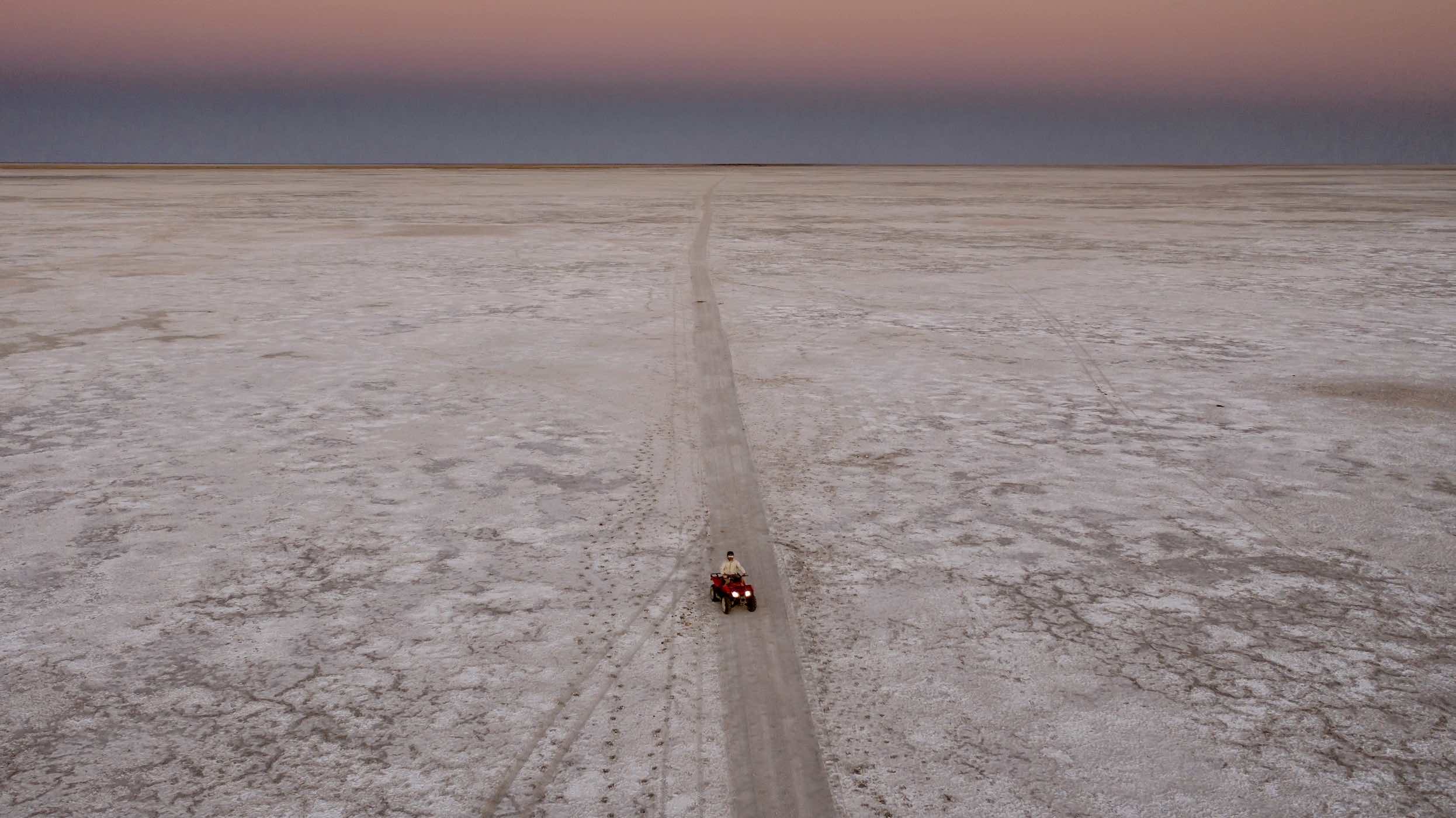 A safari vehicle on a track across the white Makgadikgadi salt pans at dusk